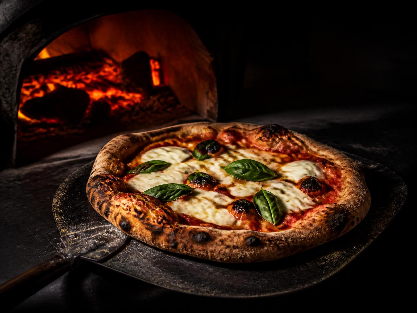 Nybakad pizza framför en glödande vedugn